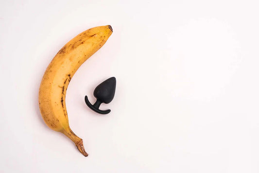 Plátano y plug anal sobre fondo blanco, representación visual de la doble estimulación y el placer íntimo