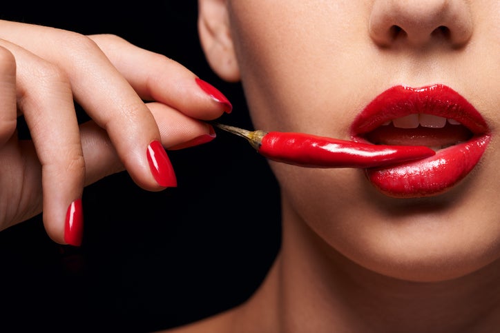 Mujer con labios rojos mordiendo un chile rojo, sensualidad y afrodisíacos naturales para potenciar el deseo sexual